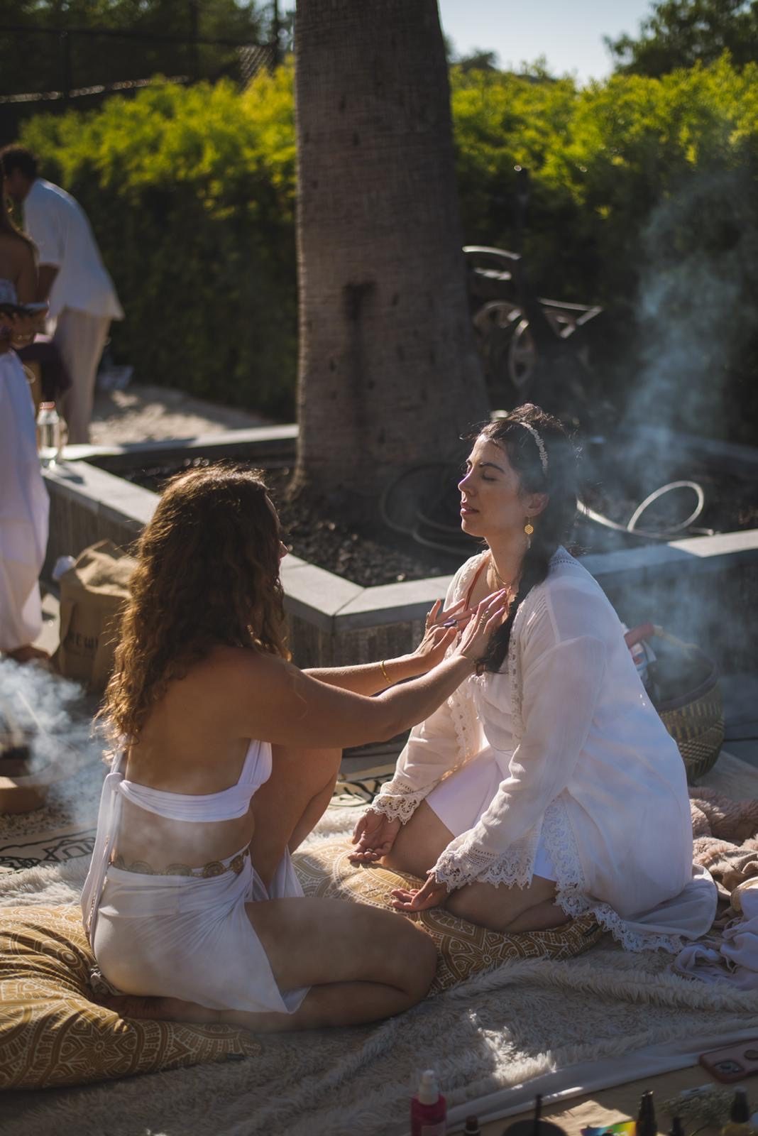 Damiana kneeling in ceremony with a woman on an outdoor altar